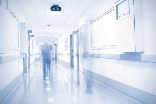 A blurred blue and white image taken from a hospital corridor, with an unidentifiable person walking in the centre.